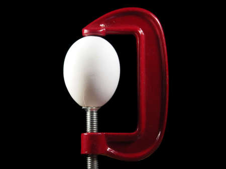 Egg in a clamp symbolizing stress or pressure. Isolated on black.の写真素材