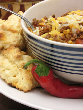 Chili with cheese and a spoon with biscuits and a chili pepper on the sideの写真素材