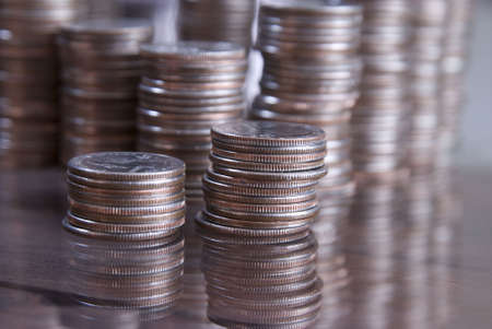 Stacks of coins on a table with reflections in the glass. Shallow depth of field focus on first stack of coins.の写真素材