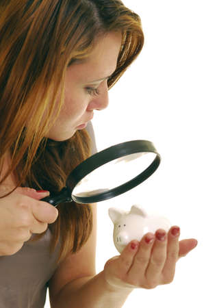 Attractive Caucasian woman looking into a piggy bank with a magnifying glass.の写真素材