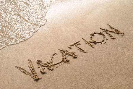 The word vacation is spelled in the sand on a beachの写真素材