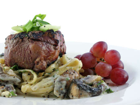 Filet mignon over pasta with grapes on a white plate isolated on white.の写真素材