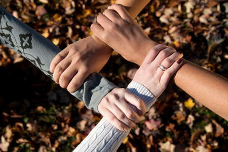 Four teens of varying nationalities grasping each other's wrists outdoors in the fallの写真素材