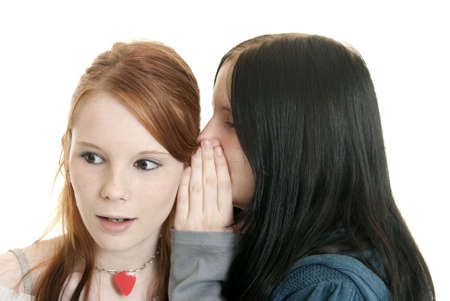 A teenage Caucasian girl whispers a secret to her sister
