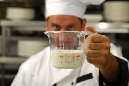 Attractive Caucasian chef looks a milk in a measuring cup. Shallow DOF. Focus on measuring cup.の写真素材