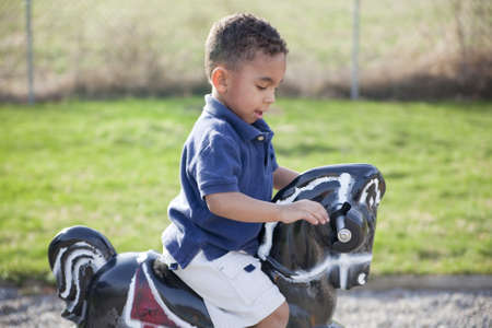 Cute multi-racial boy at the park playing on a horseの写真素材