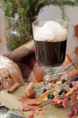 A glass of hot drink with marshmallows standing on books with sweet tasty cake behind の写真素材