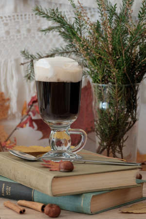 A glass of hot drink with marshmallows standing on booksの写真素材