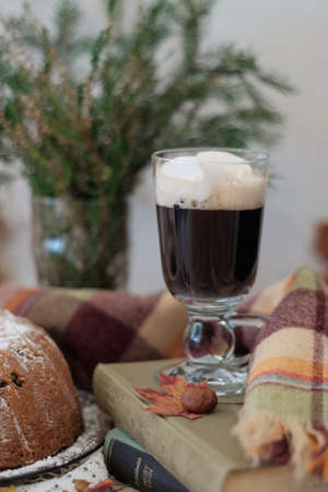 A glass of hot drink with marshmallows standing on books with sweet tasty cake behind の写真素材