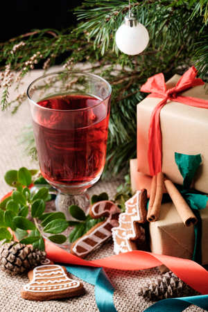 A glass of hot drink under decorative evergreen tree near wrapped gift boxesの写真素材