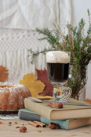 A glass of hot drink with marshmallows standing on books with sweet tasty cake behind の写真素材