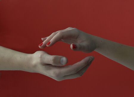 tender woman hand above a strong masculine hand on a red backgroundの写真素材