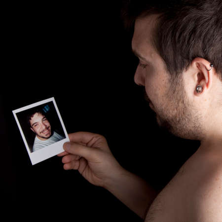 Man looking at a picture of younger himself and observing with nostalgia the passage of time の写真素材
