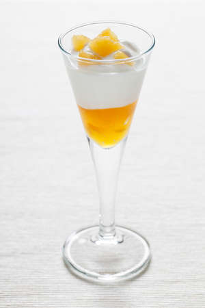Cup of yogurt with peach jam and some decorative peach pieces on a white tablecloth  の写真素材