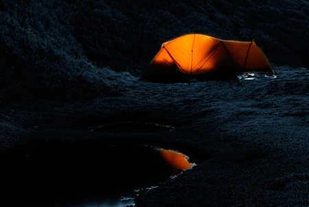 Tent in the night with weak light and small lake.の写真素材