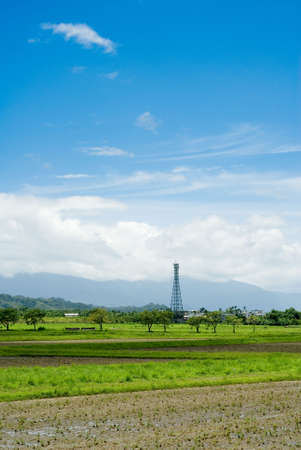 It is a tower on the green farm with blue sky.