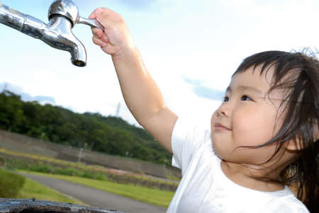She is a happy baby washing her hand and turn off faucet in the outdoor.の写真素材