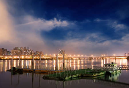 Colorful cityscape of dock with beautiful clouds on the river in the night.の写真素材