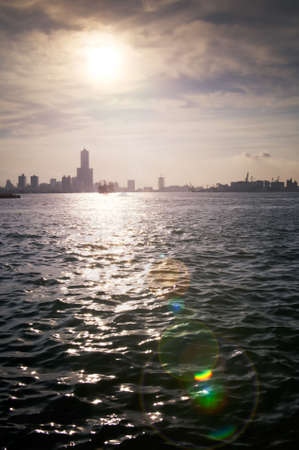 Harbor view with sun flare and buildings silhouette near ocean in Kaohsiung, Taiwan.の写真素材