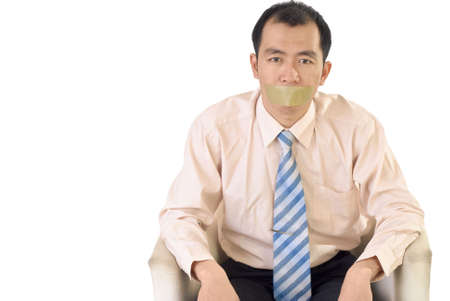 Silent businessman with tape on mouth sit on white background.の写真素材