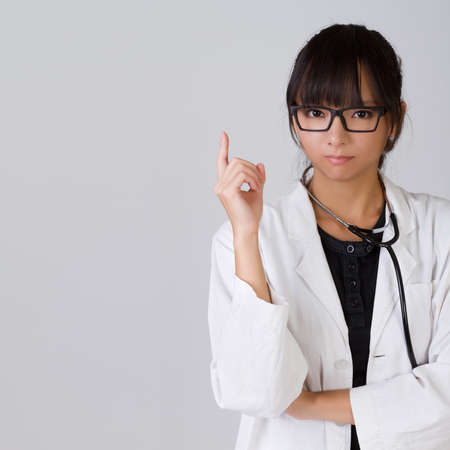 Confident Chinese medical doctor holding finger with serious expression, closeup portrait with copyspace on gray.の写真素材
