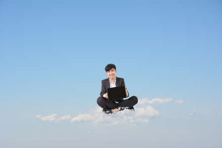Asian businessman sit on cloud and show you blank pad screen in blue sky. Concept about business, cloud, technology, pad etc. Blank pad screen on hand and copyspace on sky.の写真素材