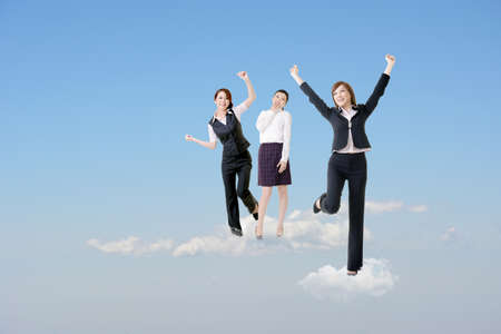 Cheerful three Asian business women stand on clouds and raise their arms feel freedom and exciting over blue sky. の写真素材