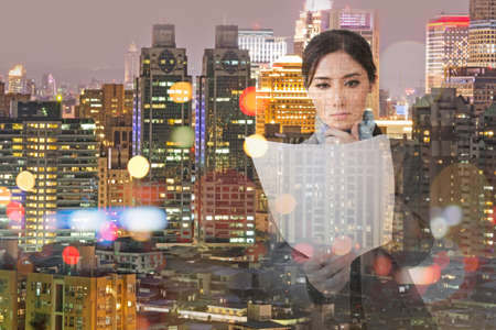 Pensive asian business woman holding file document paper next to a window with the modern city skyline reflection.の写真素材