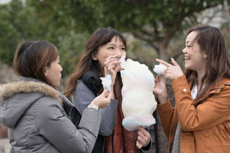 Happy young Asian woman eating cotton candy with her friends in outdoor.の写真素材