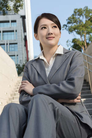 Smiling Asian business woman sit on stair of outside in modern city.の写真素材