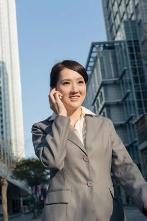 Happy Asian business woman talking on phone and walking on street in modern city of Taipei, Taiwanの写真素材