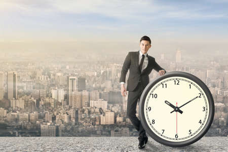 Asian businessman standing with a clock, concept of time manage or plan.