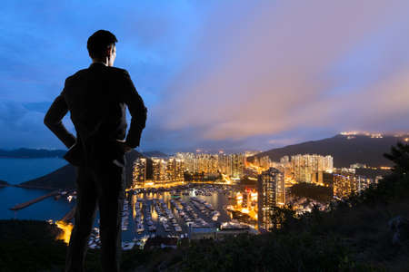 Asian businessman standing in the hill and looking at the skyscrapers and harbor in Aberdeen, Hong Kong, Asia.の写真素材
