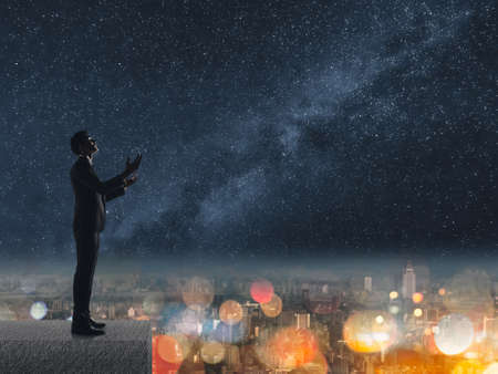 Silhouette of Asian businessman standing and praying at the roof under stars night in city.の写真素材