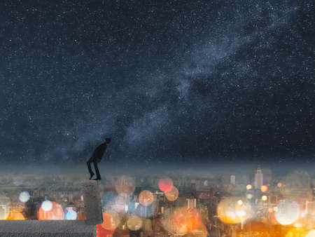 Concept of dangerous balance, business man dancing on a stone of the roof of city under stars in night.の写真素材
