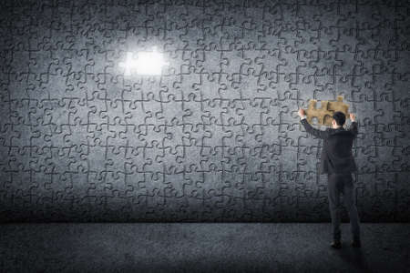 Asian business man put a piece of puzzle on the grunge wall.の写真素材
