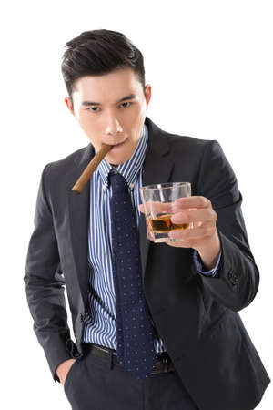 Asian young business guy with a cigar and hold a glass of whisky looking at you.の写真素材