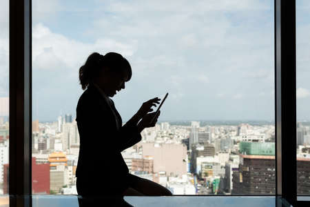 Silhouette of Asian business woman using tablet in a room, concept of technology or communication.の写真素材