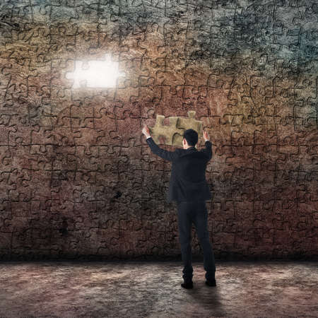 Asian business man put a piece of puzzle on the grunge wall.の写真素材