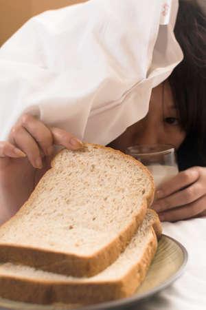 Woman's hand reaching from under duvet for breakfast in hotel.