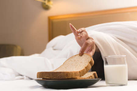 Woman's hand reaching from under duvet for breakfast in hotel.