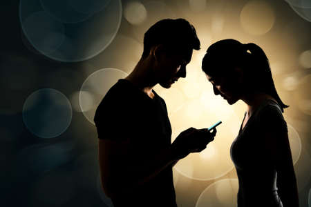 Couple using cellphone, silhouette portrait.の写真素材