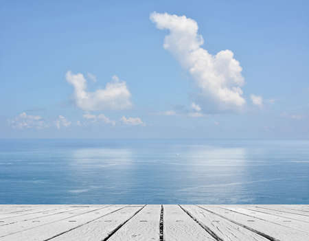 Empty wooden deck table with copyspace under sunny cloudy sky in the beach, focus on the wooden ground.の写真素材