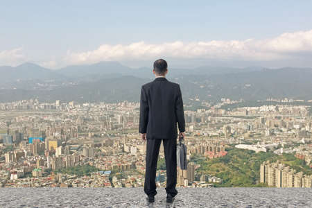 Asian business man stand and look the city under sky, concept of hard work, business, future etc.の写真素材