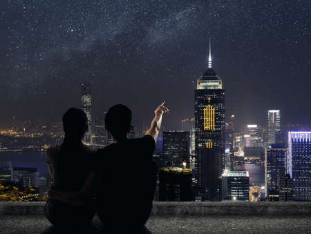 Silhouette of couple sit on ground point faraway on the roof above the city in the night.