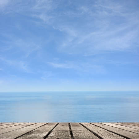 Empty wooden deck table with copyspace under sunny cloudy sky in the beach, focus on the wooden ground.の写真素材