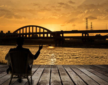 Silhouette of businessman sit on chair and hold a cigar and looking at the city in night.の写真素材