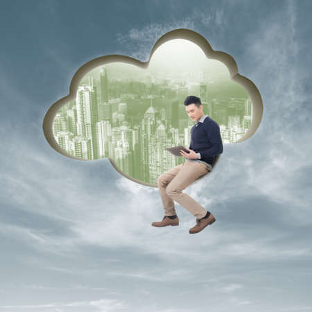 Cloud concept with man sit at a cloud shaped wall and using tablet.