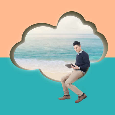 Cloud concept with man sit at a cloud shaped wall and using tablet.の写真素材