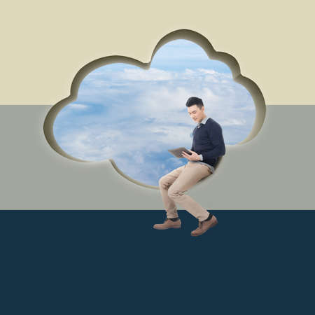 Cloud concept with man sit at a cloud shaped wall and using tablet.